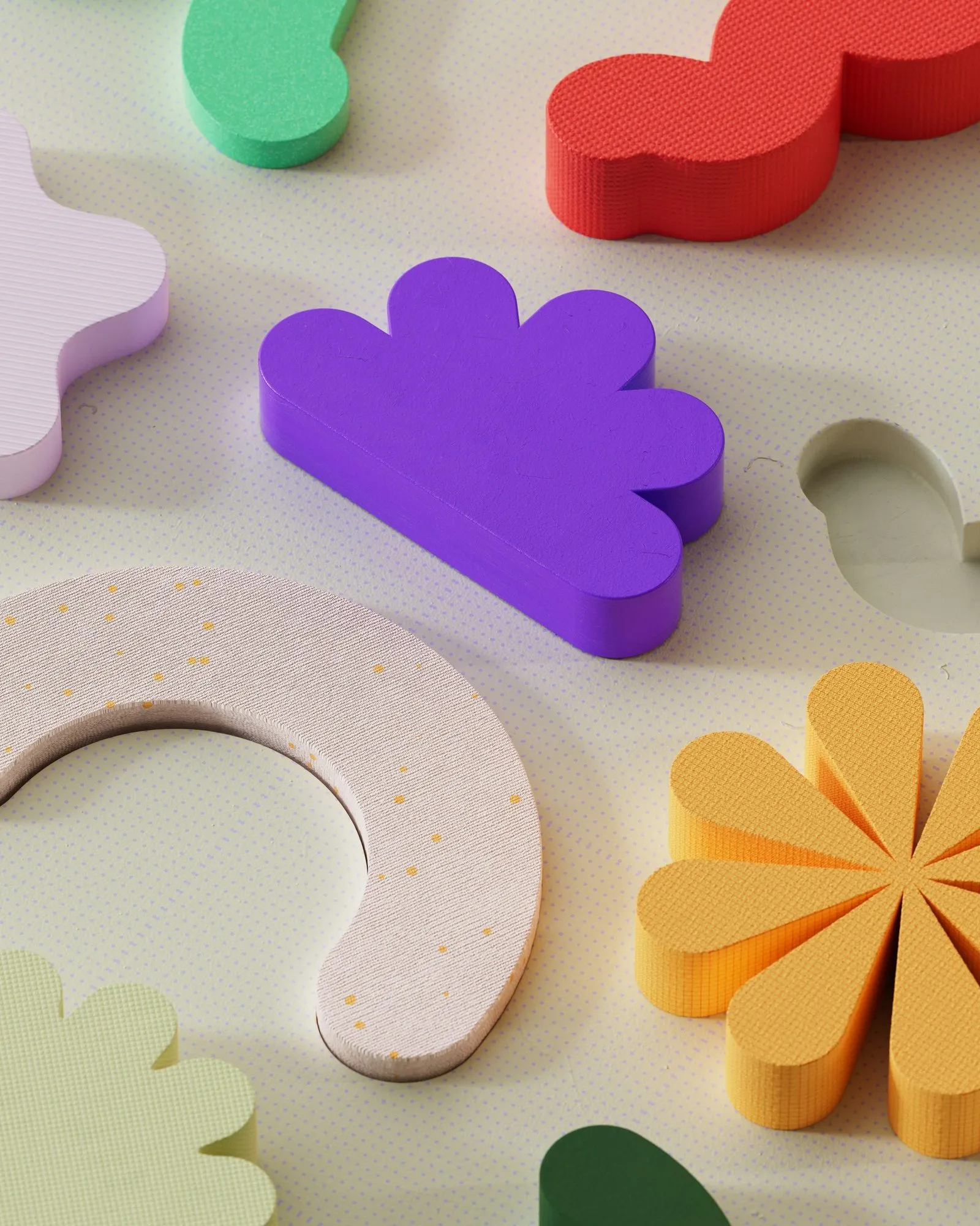 Colorful clay shapes – a purple cloud, an orange flower and a pink ring – arranged on a beige surface