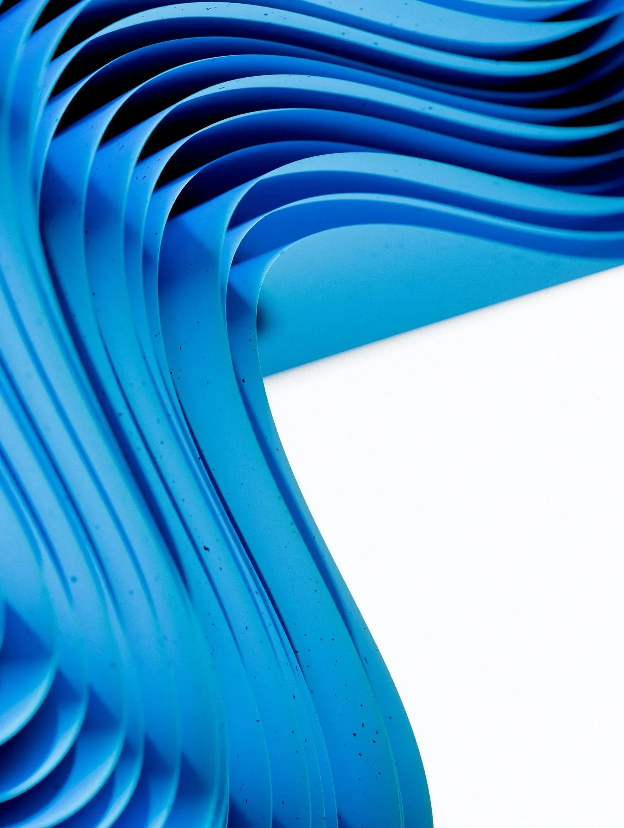 Layered sheets of blue paper curving in waves beside a clean white surface