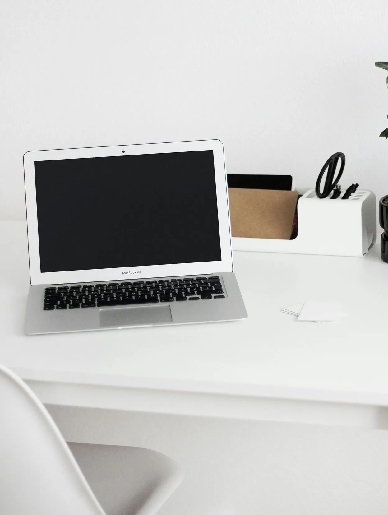 Open silver laptop with a blank screen on a bright white desk next to a desk organiser