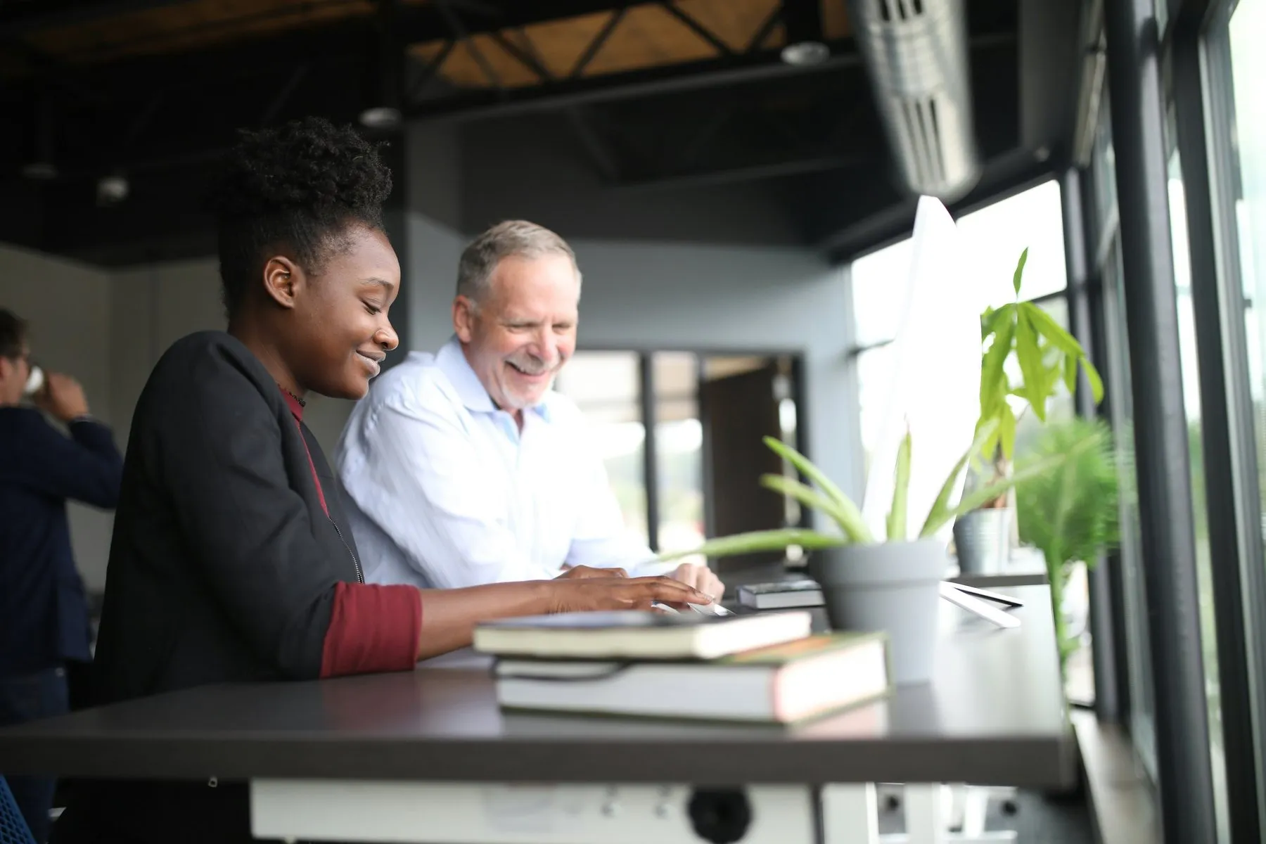 Two colleagues smiling at a laptop at a standing desk in a bright office