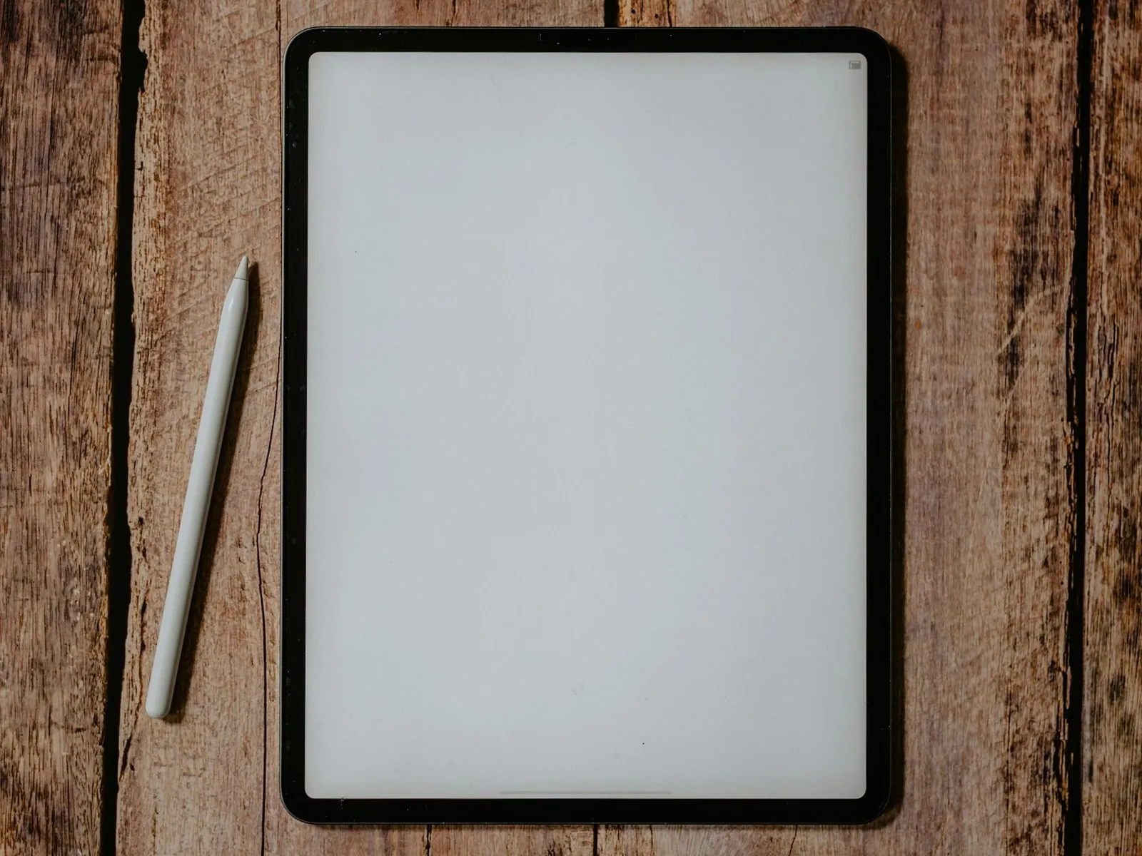 Tablet with a blank white screen and a stylus lying on a weathered wooden desk