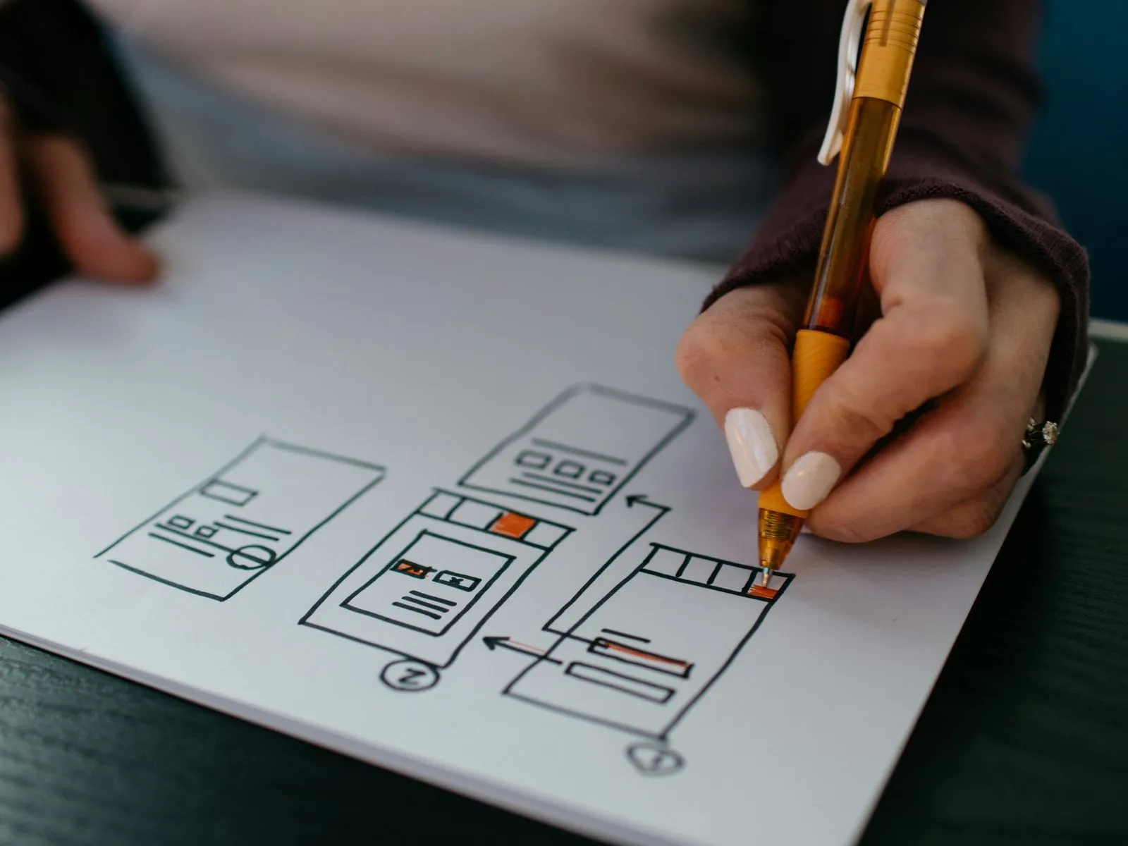 Hand sketching app wireframes with an orange pen on white paper