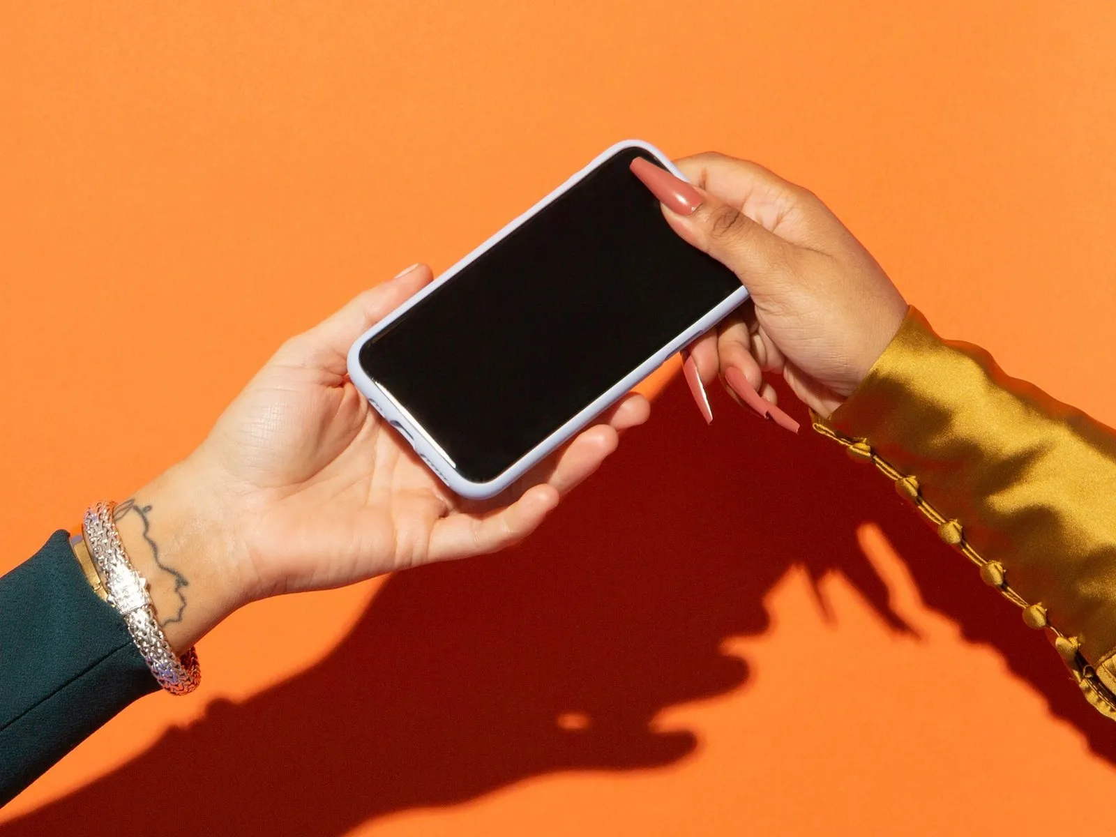 Two hands passing a smartphone with a blank black screen against an orange background