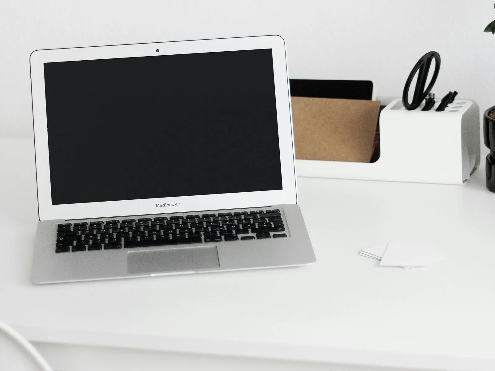 Open silver laptop with a blank screen on a bright white desk next to a desk organiser